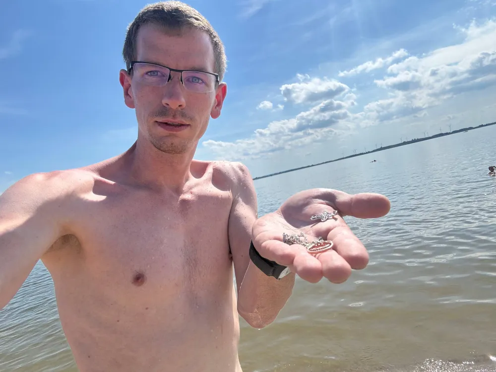 Mann im flachen Wasser des Dümmer Sees zeigt auf seiner Handfläche zwei Ringe, einen Kreuzanhänger und eine Kette.