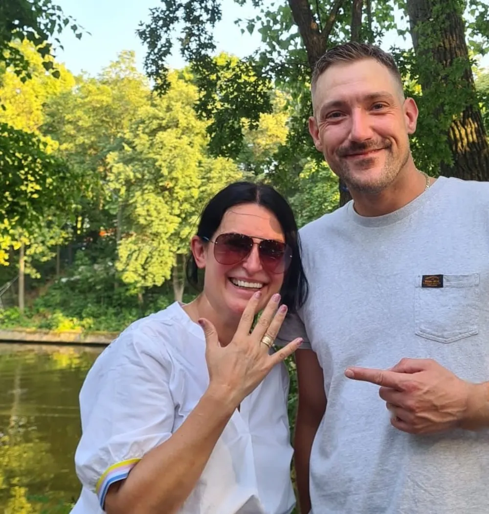 Frau und Mann am Ufer des Plötzensees, die Frau zeigt lächelnd ihre Hand mit dem zurückgegebenen Goldring.