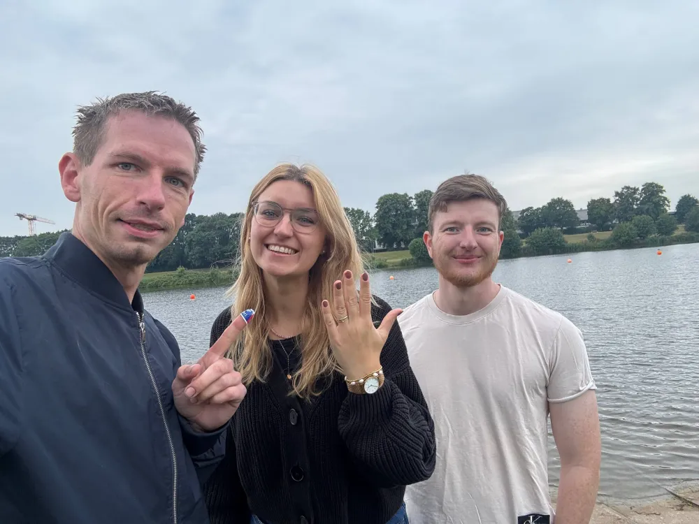 Ehepaar am Ufer des Werdersees, die Frau zeigt lächelnd ihre Hand mit dem zurückgegebenen Ehering.